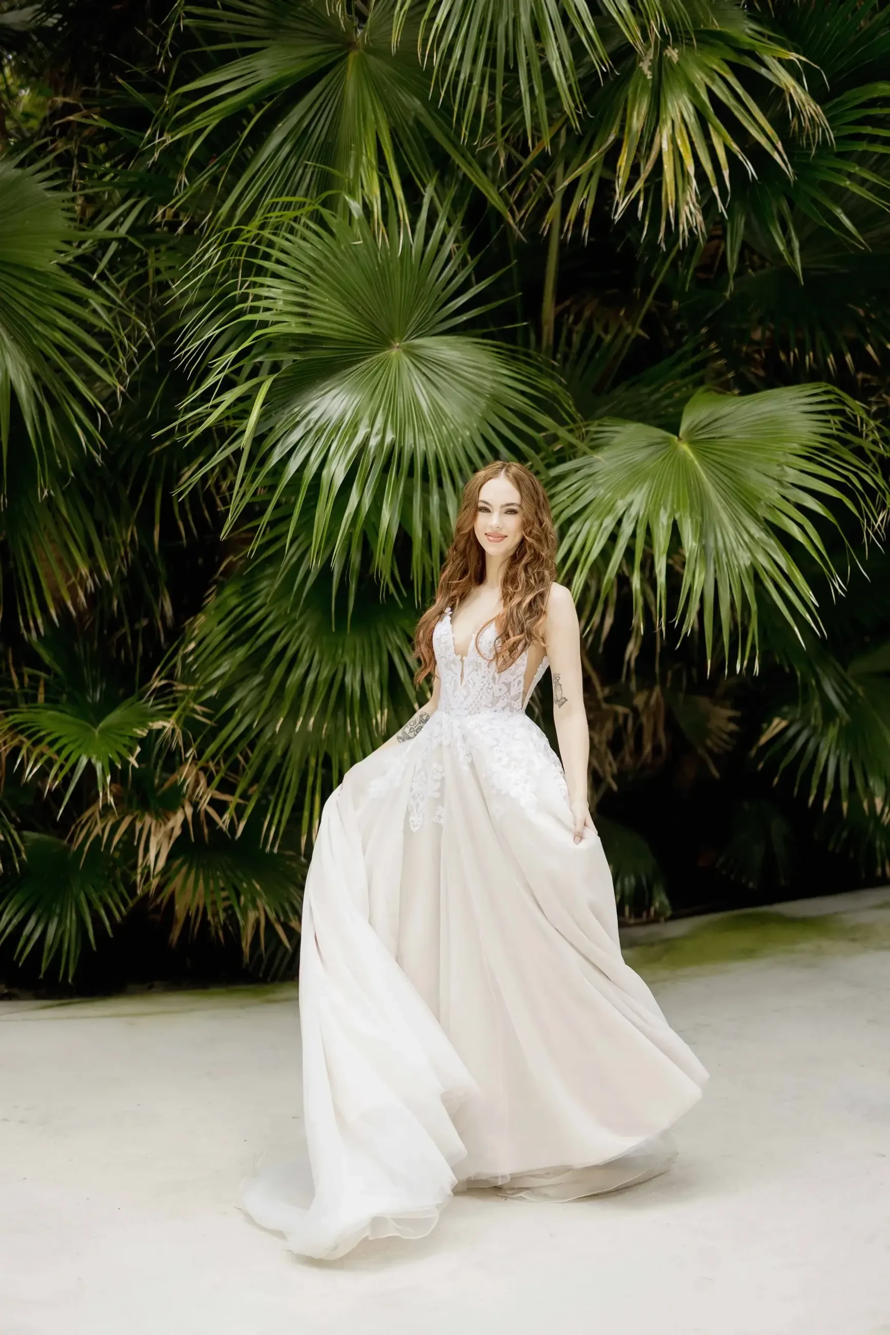 A woman in a white gown standing amidst lush green palm plants.