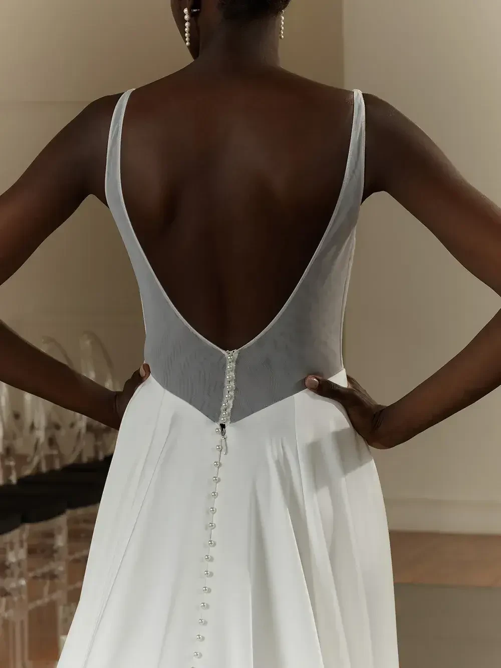 A woman wearing a sleeveless white dress with a low back and a gray panel. The dress has a row of buttons running down the back.