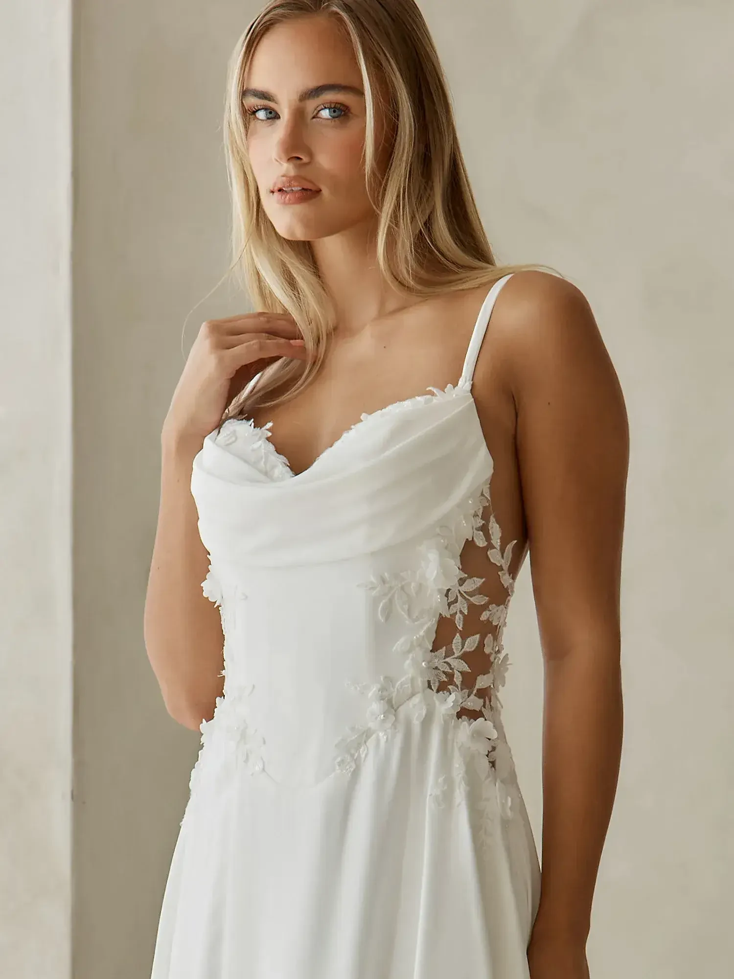 A woman wearing a white dress with floral detailing, standing against a neutral background.